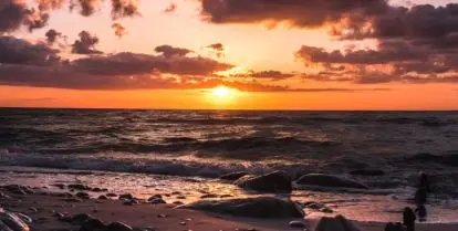 sand with stones near water and colorful sunset sky