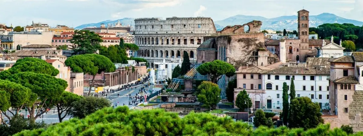 trees, modern buildings, and ancient ruins with mountains in background