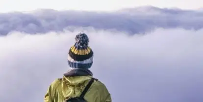 person wearing winter hat and backpack looking through lavender clouds