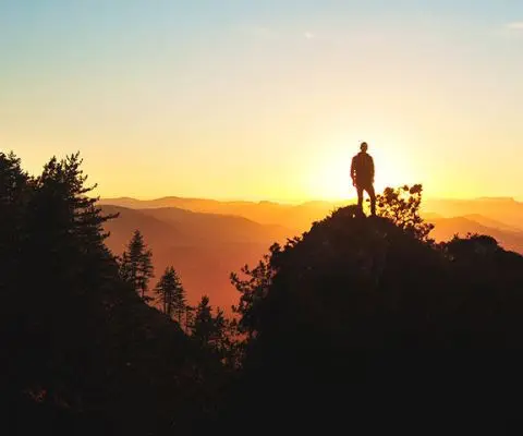 Silhouette of person standing on rock in front of warm sunrise in Oairsun, Spain