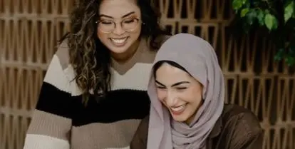 two smiling people looking at tablet device while one sits and the other stands