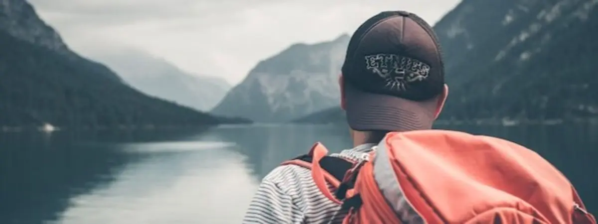 back of person wearing a backpack as they look out on water and mountains