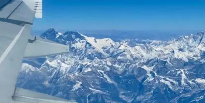 airplane wing over clouds and mountain peaks