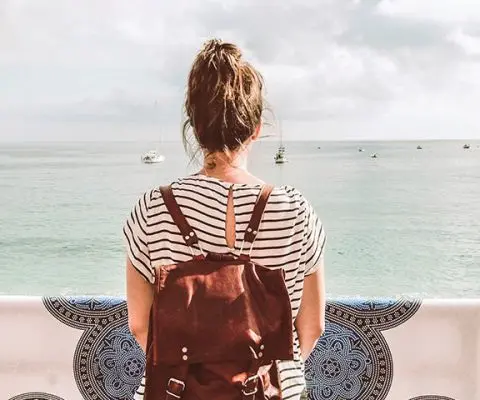 woman in black and white striped shirt with bun and red backpack looking at ocean