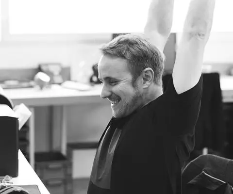 man sitting at desk stretching and smiling