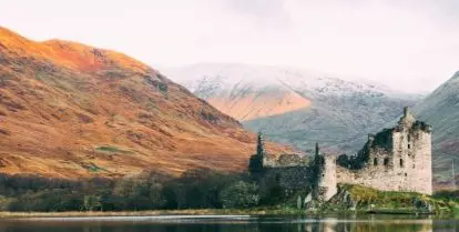 gray castle next to water with mountains and clouds behind