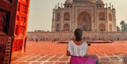 person standing under archway opening up to view of Taj Mahal